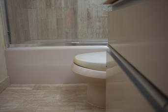 cabinets, a toilet, and a bathtub with glass door, lit by white light